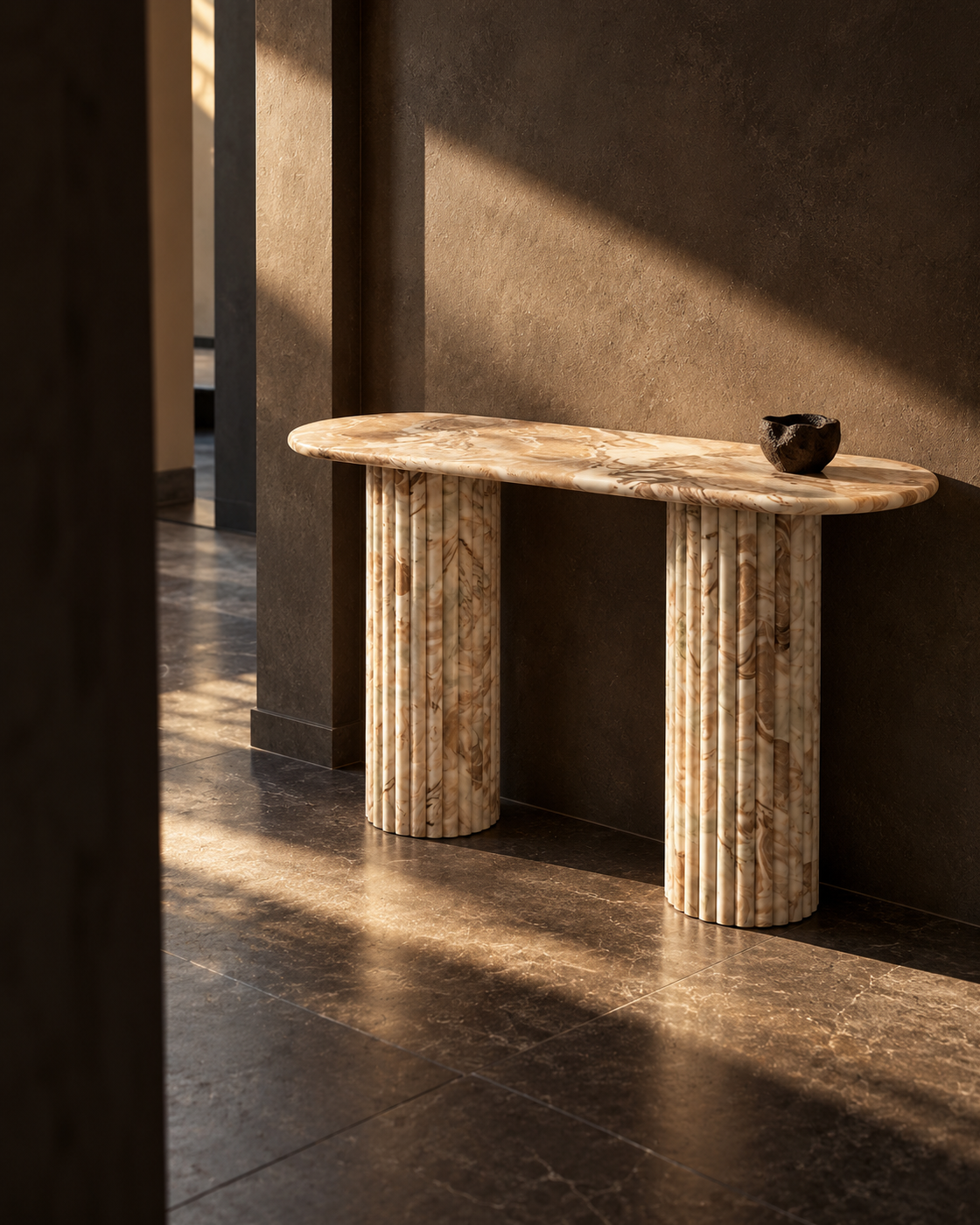Tan marble console table framed by dark architectural walls with a shaft of sunlight and deep shadows