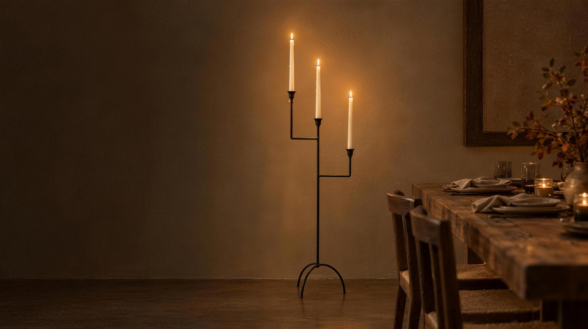 Bardot hammered iron floor candelabra with three stepped lit tapers beside an autumn dinner table